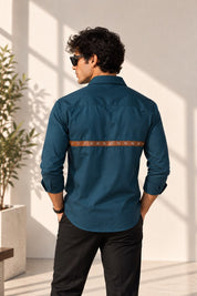 Aachari navy teal cotton shirt featuring a back leather strap with metallic eyelets worn by a man in a bright room.